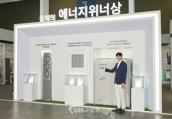 2019 대한민국 에너지대전 삼성전자 부스에서 전시회 최고상인 에너지 대상 및 국무총리상을 수상한 시스템에어컨 4Way 카세트 냉난방기와 에너지 위너상을 받은 DVM-S 고온형 시스템에어컨을 배경으로 모델이 포즈를 취하고 있다